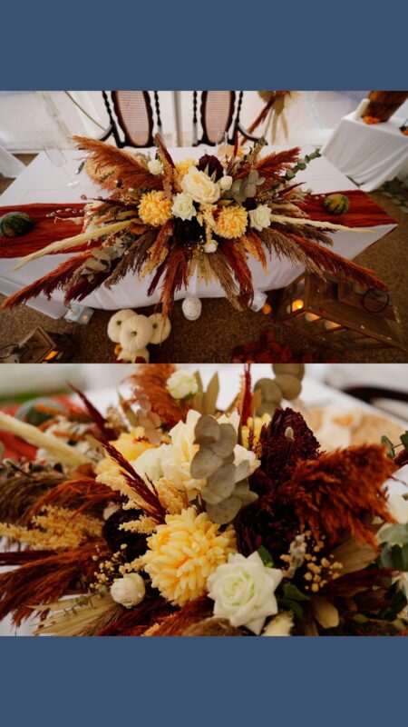 Top table arrangement for autumn wedding with yellow, orange and white colours. There is pampas grass, palms and yellow and white flowers.