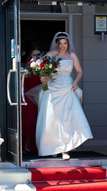Bride walks out with her bouquet of red and white flowers.