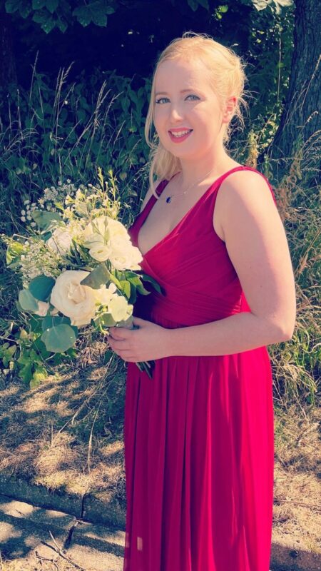 Bridesmaid in red dress holds oval bouquet of white roses.