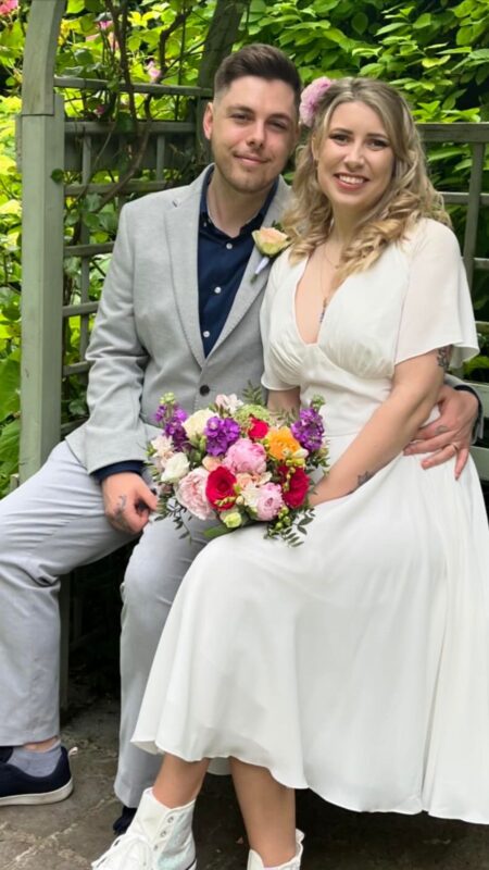 Bride and groom sitting. Bride holds colourful bouquet.
