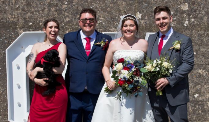 Bride and Groom with their friends on their wedding day. The bride holds a bouquet of red and white flowers.
