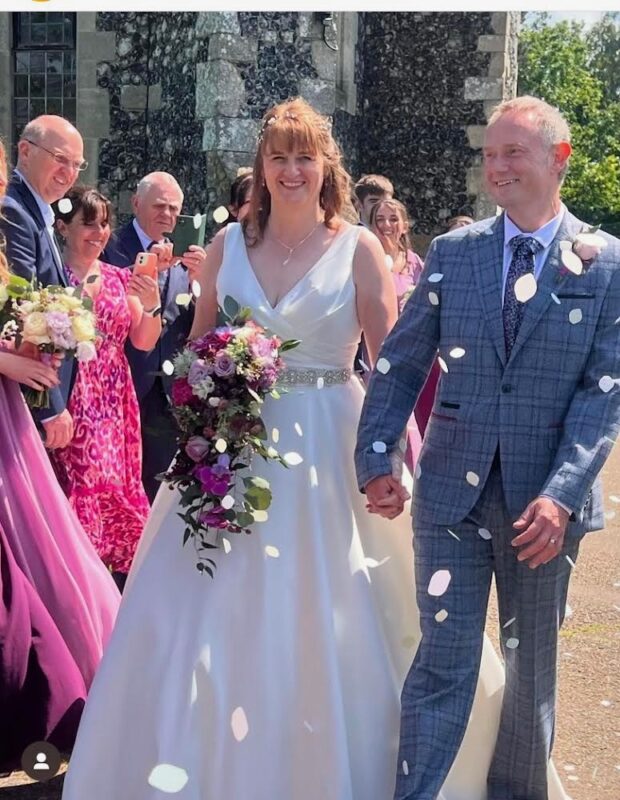 Bride and Groom walk under confetti. We see her cascade bouquet clearly with various flowers in it including roses, Canterbury bells and peonies.