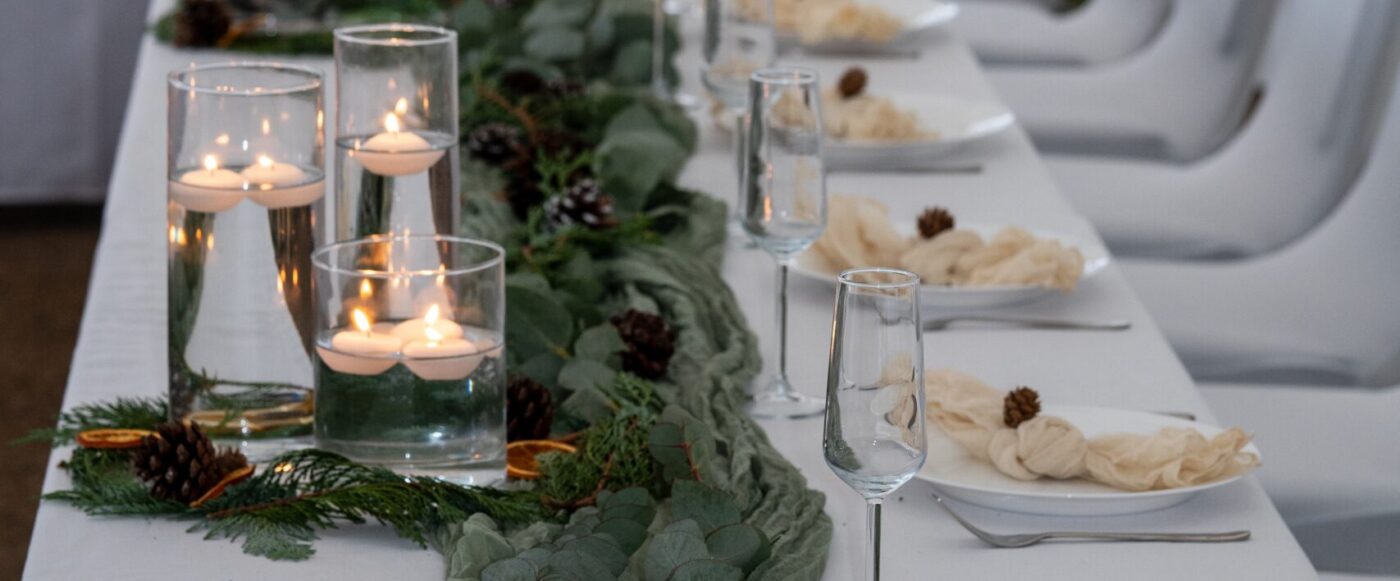 Winter wedding table set up. Sage runners, white plates, pinecones, hurricane vases with floating candles.