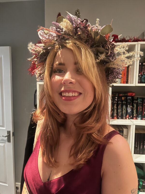 A woman wears a flower crown of dried flowers. There are purple and brown tones.